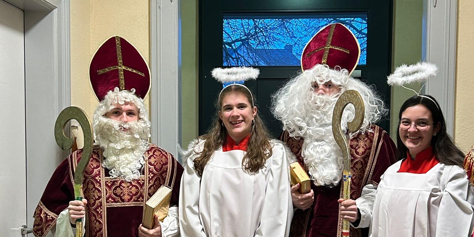 Zwei Personen als Bischöfe und zwei als Engel in festlichen Gewändern stehen zusammen in einem Flur. (c) Heike Dixius Zwei Personen als Bischöfe und zwei als Engel in festlichen Gewändern stehen zusammen in einem Flur.