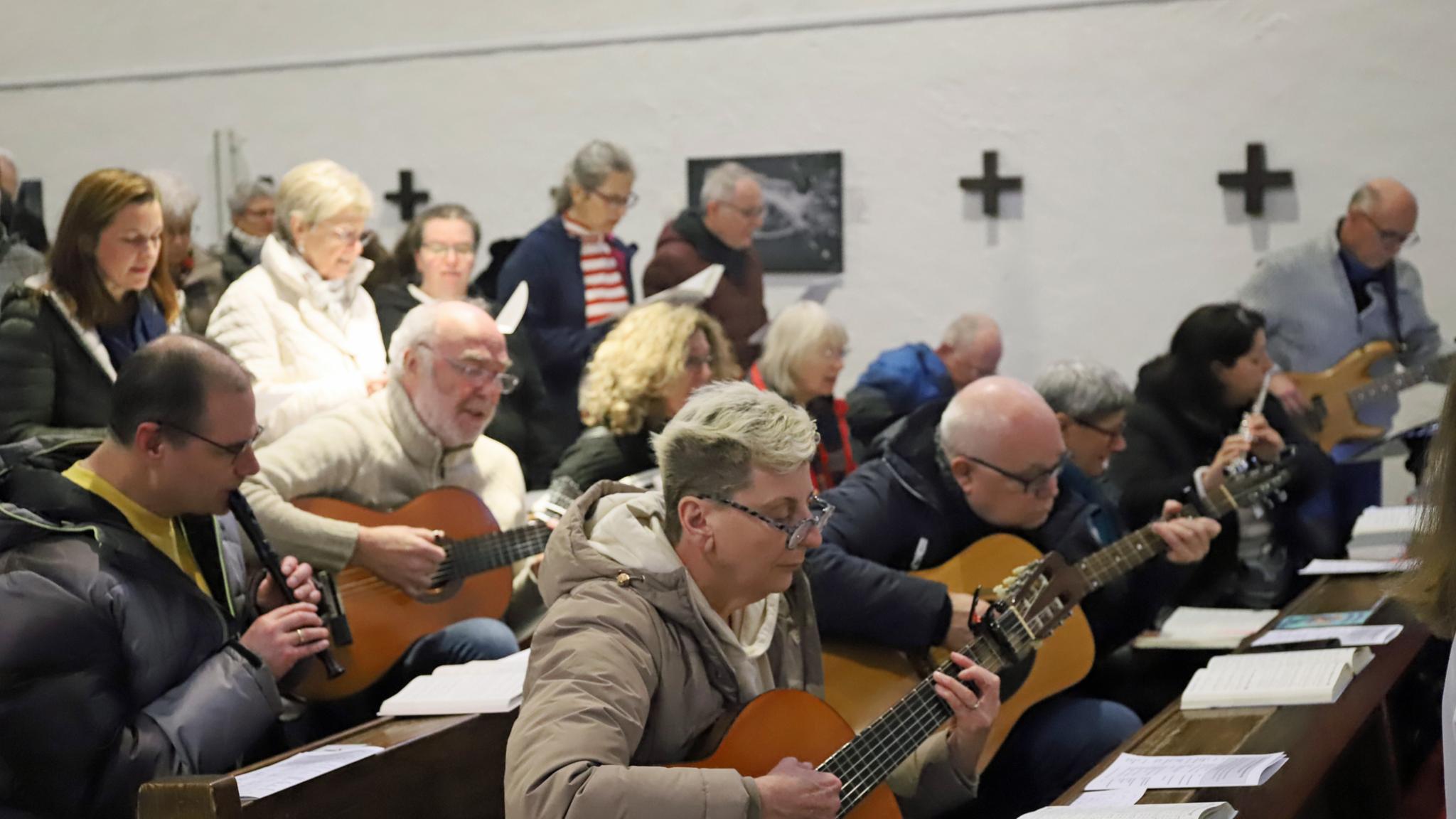 Eine Gruppe von Personen sitzt in Kirchenbänken und spielt gemeinsam Musikinstrumente während einer Veranstaltung in einem kirchlichen Raum.