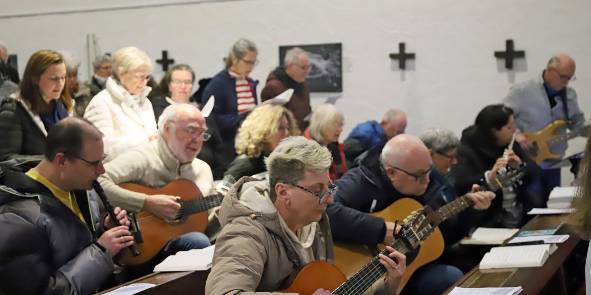 Eine Gruppe von Personen sitzt in Kirchenbänken und spielt gemeinsam Musikinstrumente während einer Veranstaltung in einem kirchlichen Raum.