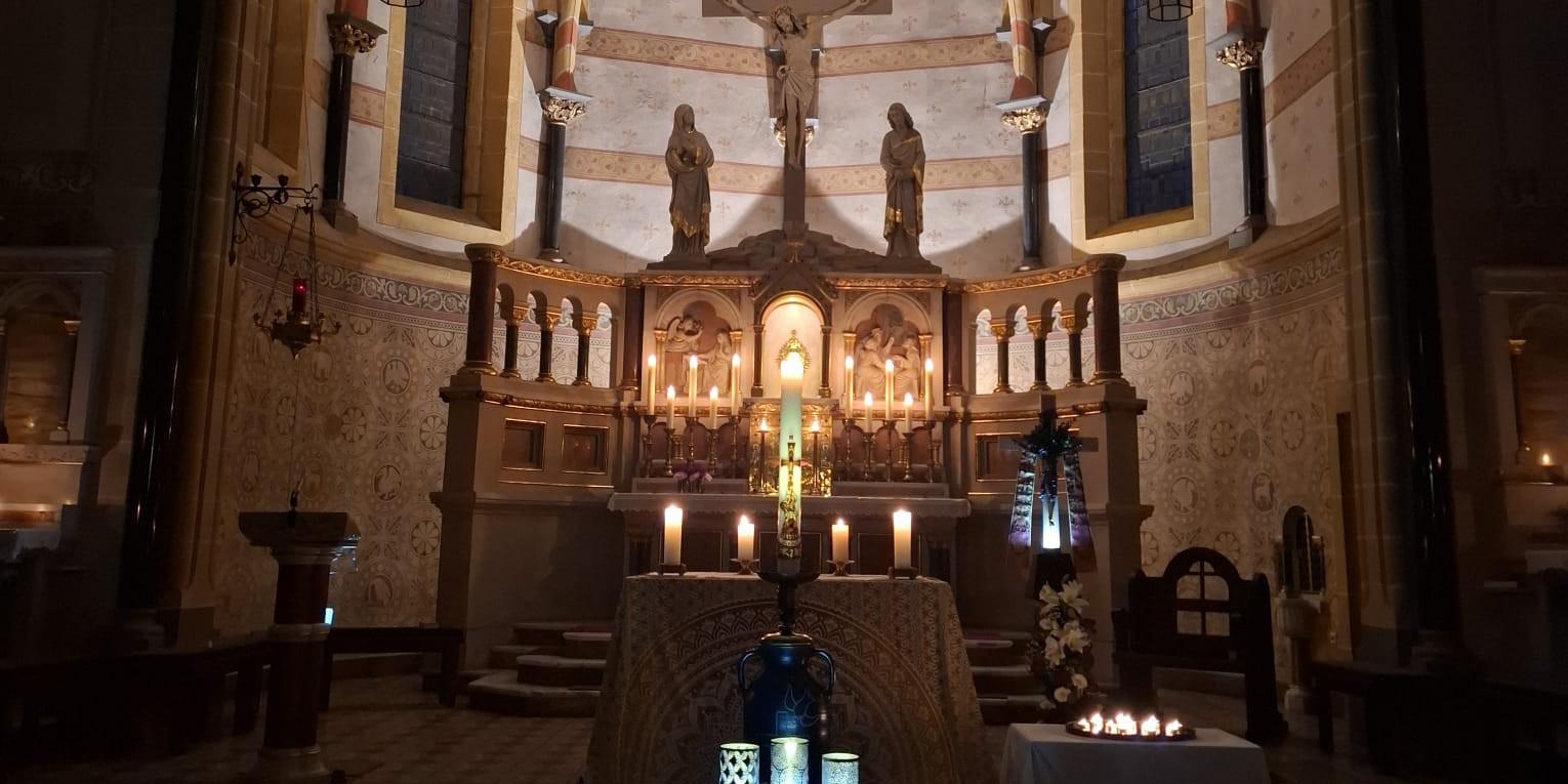 Ein festlich beleuchteter Kirchenaltar mit Kerzen und Kreuz im Zentrum.