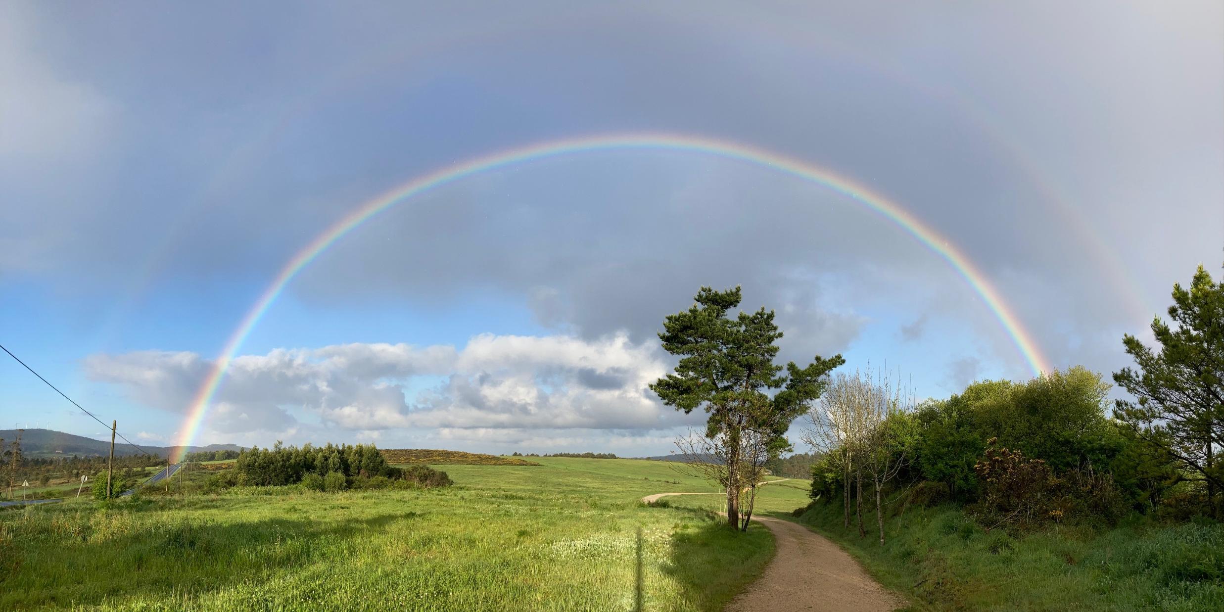 Ein weiter Regenbogen spannt sich über eine grüne Landschaft mit Feldern, Weg und einzelnen Bäumen. (c) Josef Weber Ein weiter Regenbogen spannt sich über eine grüne Landschaft mit Feldern, Weg und einzelnen Bäumen.