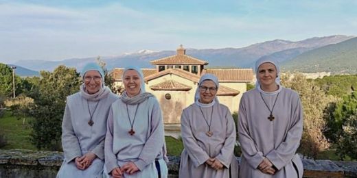 Vier Ordensschwestern vor einem Kloster in bergiger Landschaft.