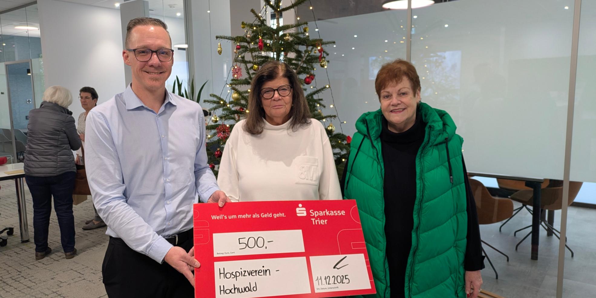 Das Foto zeigt eine Spendenübergabe in einem modernen Innenraum mit Weihnachtsdekoration. Im Vordergrund halten drei Personen einen großen symbolischen Scheck der Sparkasse Trier. (c) Ambulantes Hospiz Hochwald Das Foto zeigt eine Spendenübergabe in einem modernen Innenraum mit Weihnachtsdekoration. Im Vordergrund halten drei Personen einen großen symbolischen Scheck der Sparkasse Trier.