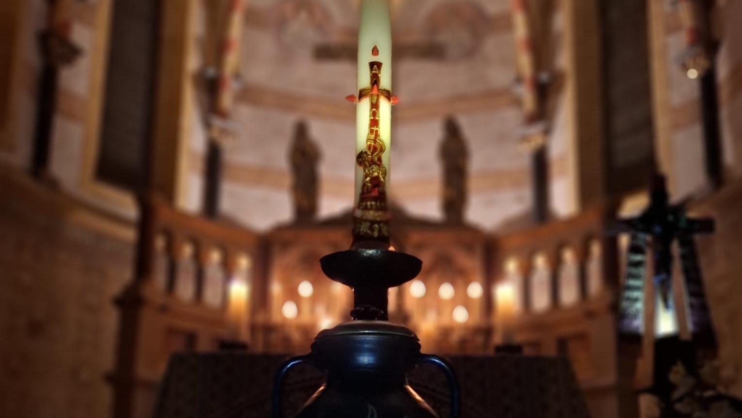 Eine brennende Kerze im Vordergrund, dahinter der festlich beleuchtete Innenraum einer Kirche.