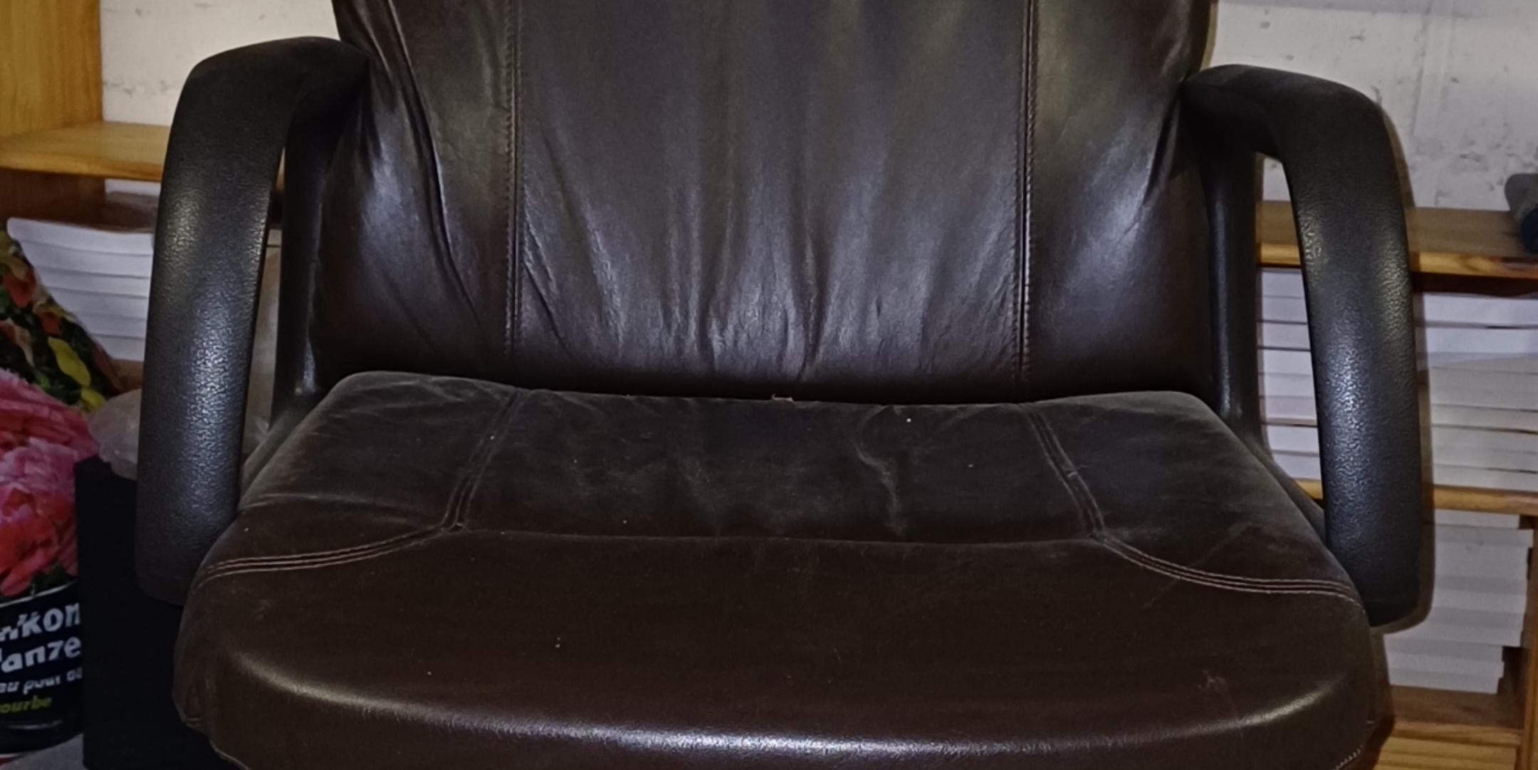 Der Stuhl ist aus braunem Leder gefertigt, hat Armlehnen und steht auf einem stabilen Metallgestell.