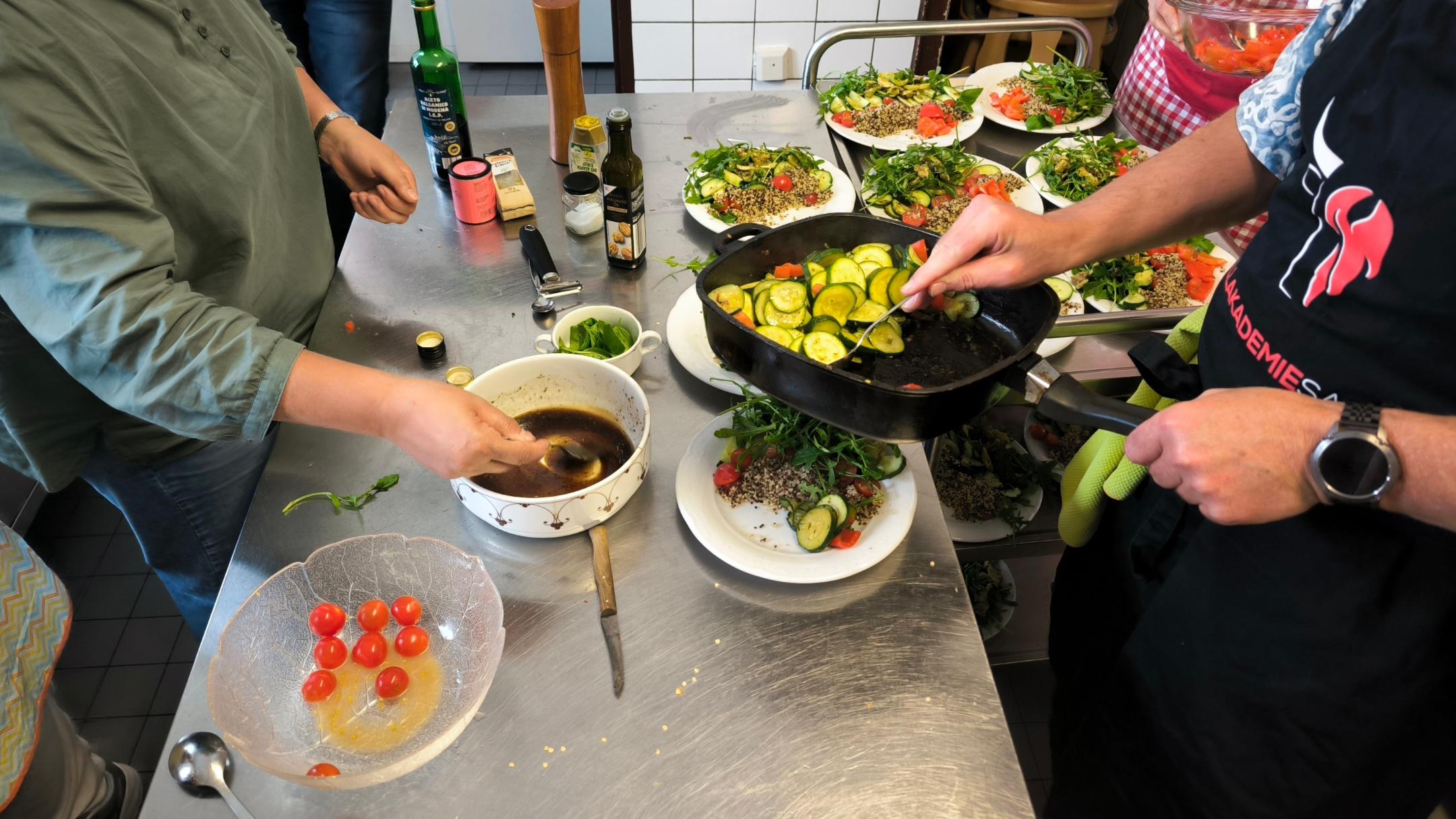 Auf dem Tisch liegen zahlreiche frische Zutaten, und im Vordergrund steht eine große Schale mit Cherrytomaten.