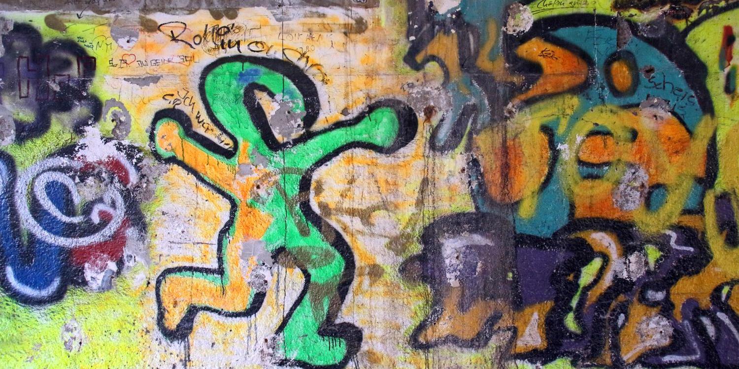 Eine bunte Wand mit lebhaftem Graffiti, darunter eine tanzende, grün umrandete Figur.
