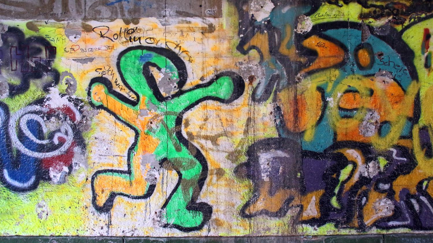 Eine bunte Wand mit lebhaftem Graffiti, darunter eine tanzende, grün umrandete Figur.