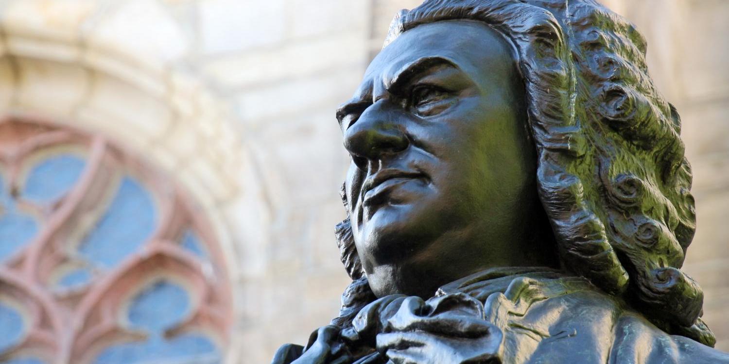 Bronzestatue eines Mannes mit Lockenperücke vor einer Kirche