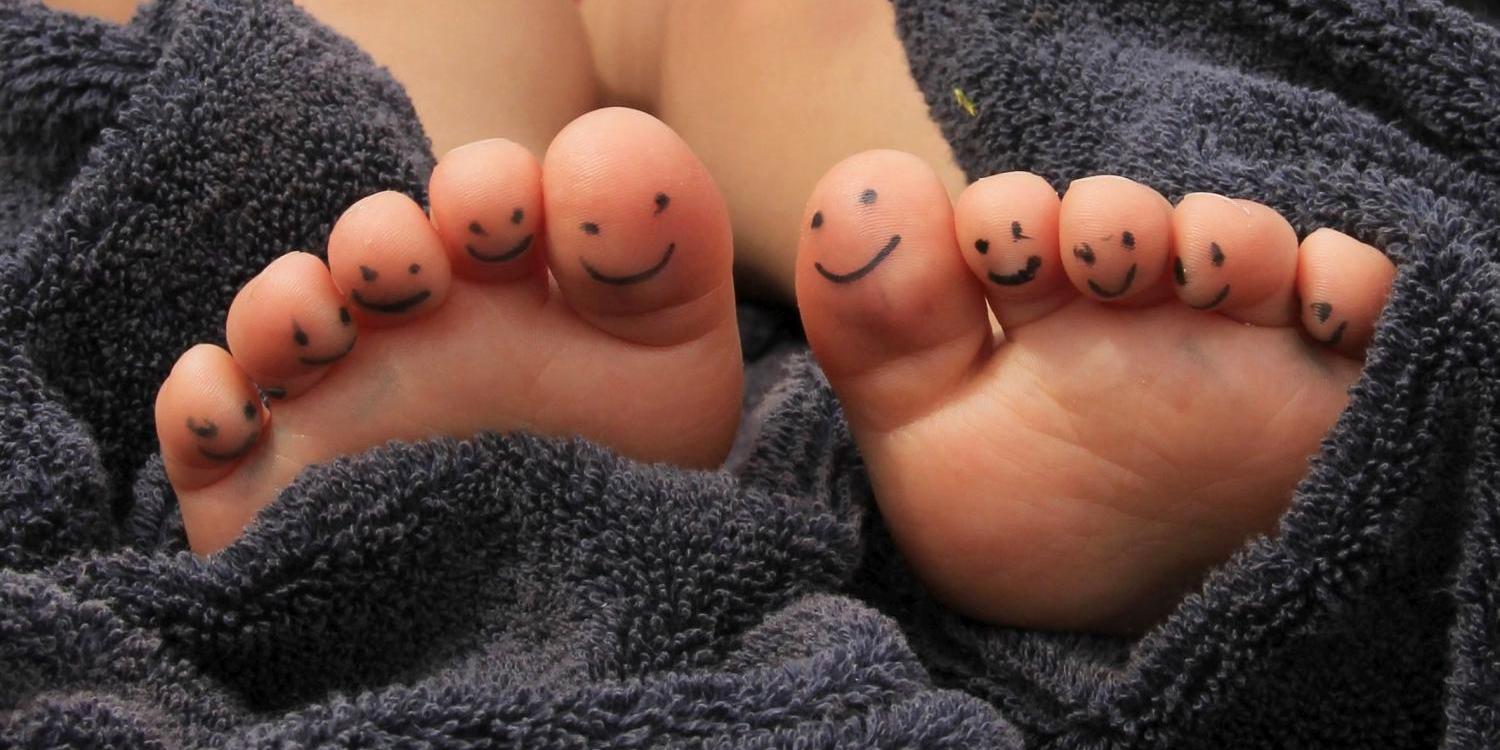 Zwei Füße liegen in einem Handtuch, und auf den Zehen sind kleine lächelnde Gesichter gemalt.