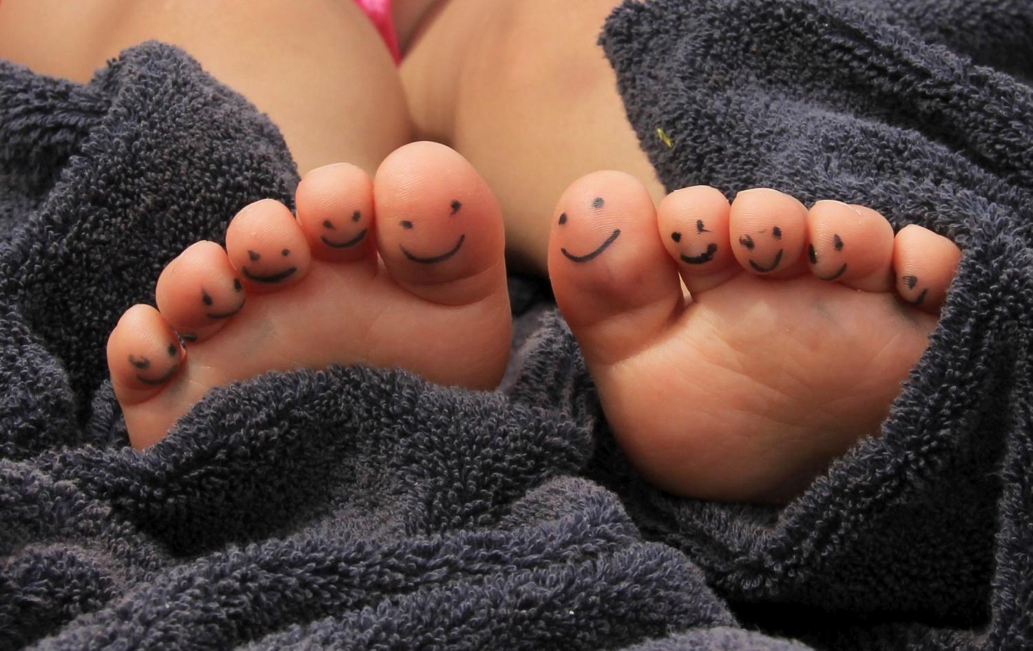 Zwei Füße liegen in einem Handtuch, und auf den Zehen sind kleine lächelnde Gesichter gemalt.