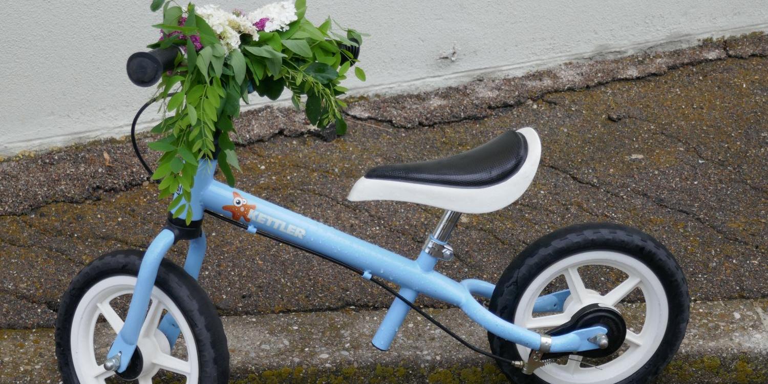 Blaues Kinderlaufrad mit Blumen am Lenker auf Gehweg abgestellt.