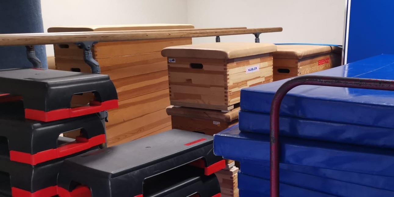 Gestapelte Turnmatten, Sprungkästen und weitere Sportgeräte in einem Geräteraum.