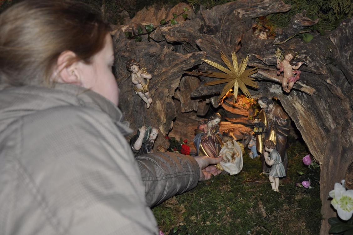 Das Bild zeigt ein Kind, das eine Figur in eine liebevoll gestaltete Weihnachtskrippe mit der Heiligen Familie, Engeln und einem goldenen Stern legt.