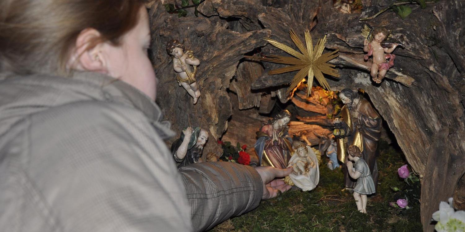 Das Bild zeigt ein Kind, das eine Figur in eine liebevoll gestaltete Weihnachtskrippe mit der Heiligen Familie, Engeln und einem goldenen Stern legt.