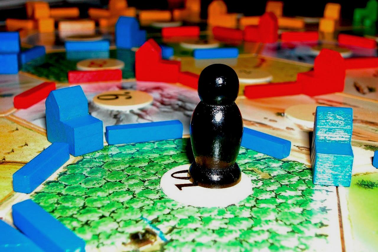 Das Foto zeigt ein Spielbrett mit sechseckigen Feldern, bunten Holzspielsteinen und einer schwarzen Spielfigur auf einem grünen Feld mit der Zahl 10.