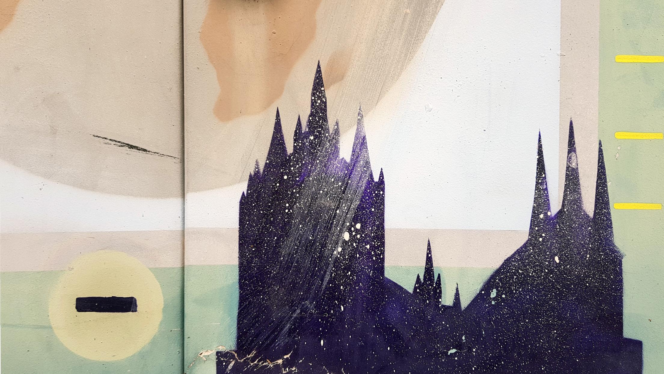 Das Foto zeigt eine Wandmalerei mit der Silhouette einer Kirche vor einem abstrakten Hintergrund aus geometrischen Formen und einem großen Kreis.