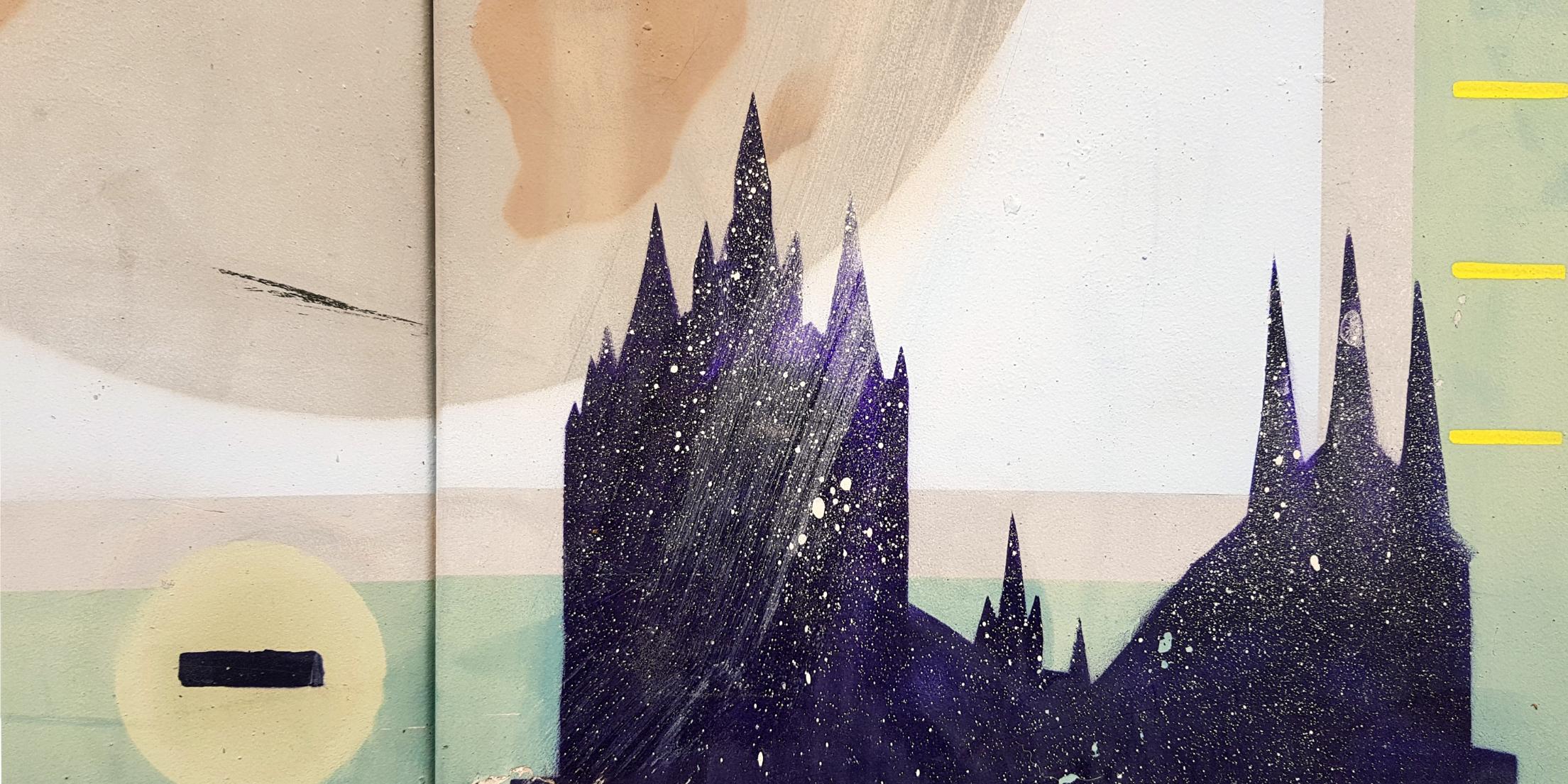 Das Foto zeigt eine Wandmalerei mit der Silhouette einer Kirche vor einem abstrakten Hintergrund aus geometrischen Formen und einem großen Kreis.