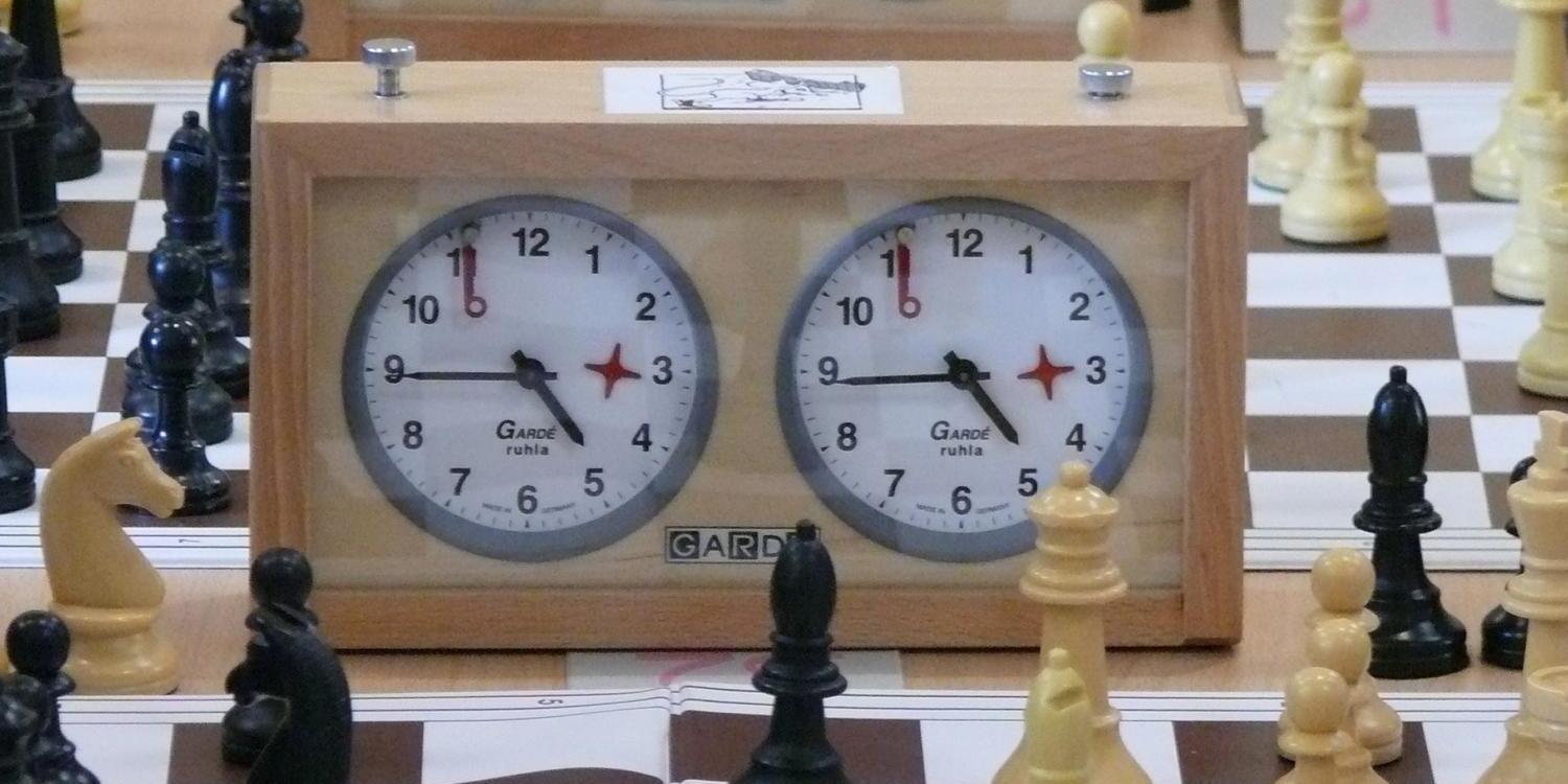 Auf dem Bild sind mehrere Schachbretter mit Figuren und klassischen Schachuhren zu sehen.