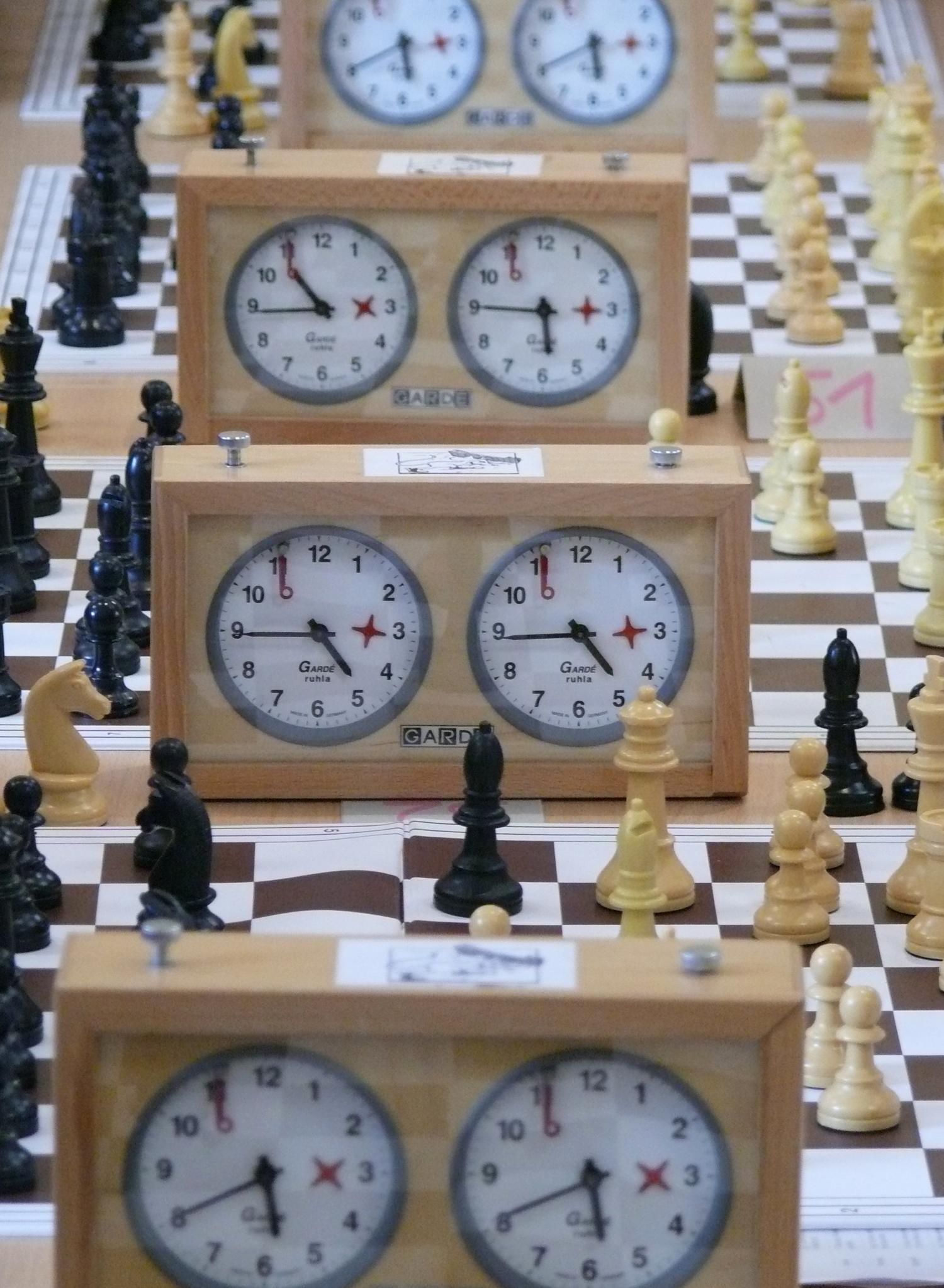 Auf dem Bild sind mehrere Schachbretter mit Figuren und klassischen Schachuhren zu sehen.