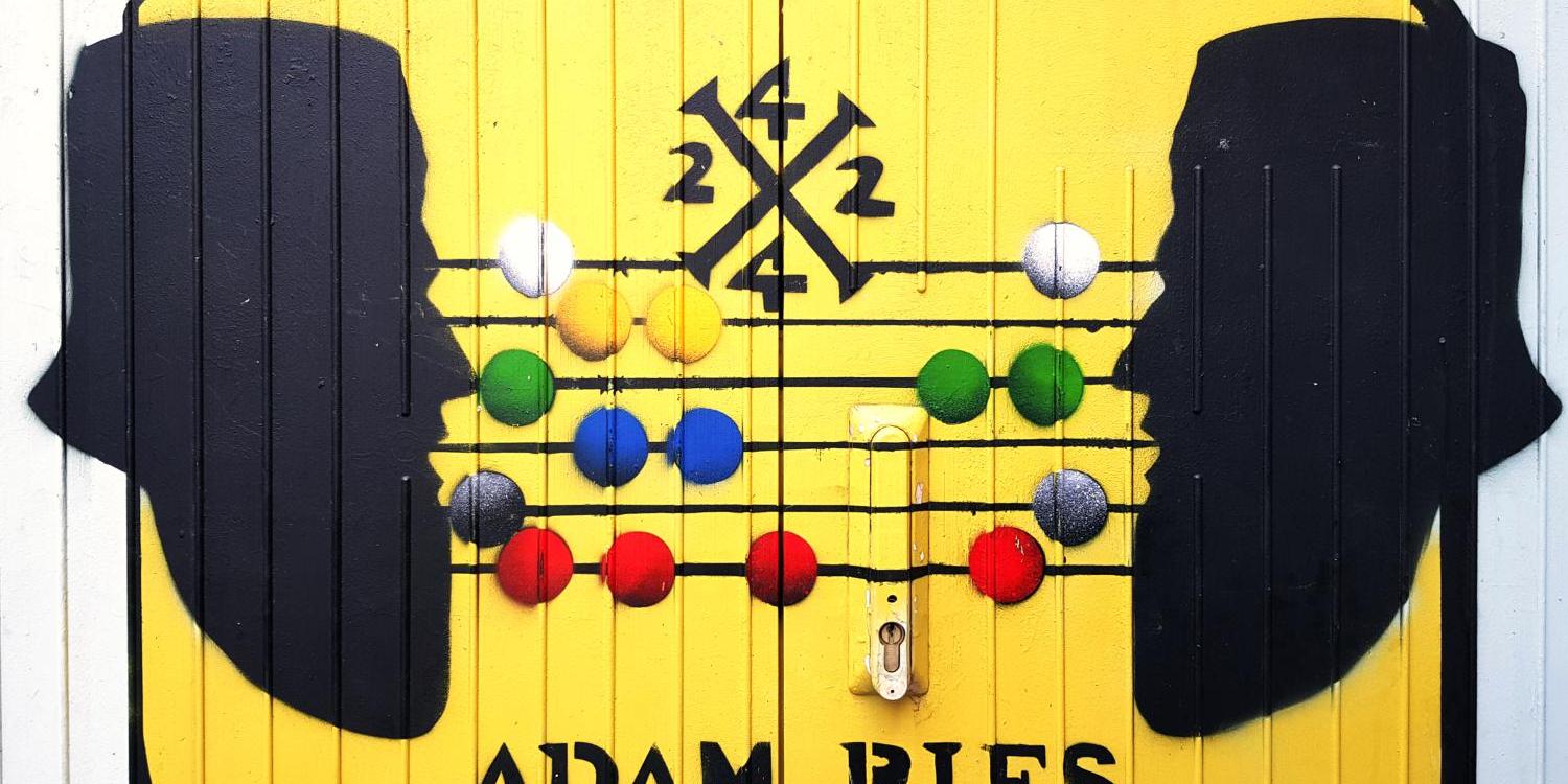 Gelbes Bild mit zwei schwarzen Kopf-Silhouetten und einem bunten Abakus, darunter der Schriftzug ‚Adam Ries‘.