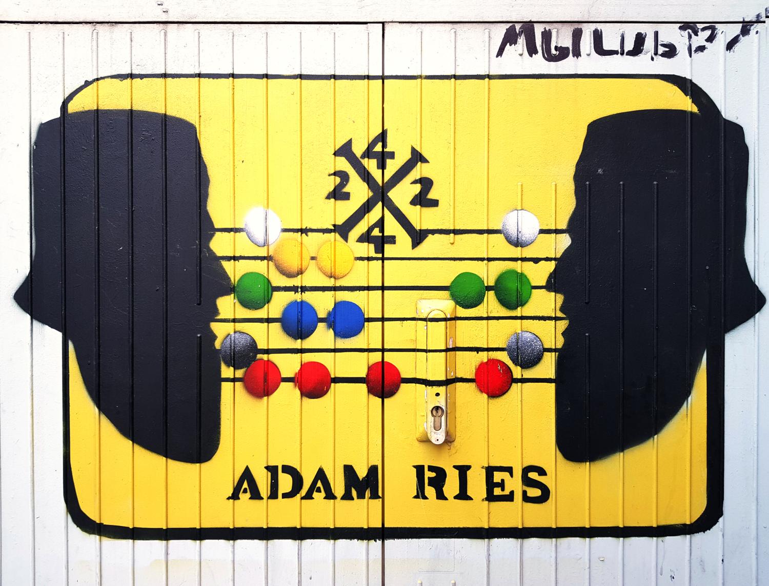 Gelbes Bild mit zwei schwarzen Kopf-Silhouetten und einem bunten Abakus, darunter der Schriftzug ‚Adam Ries‘.