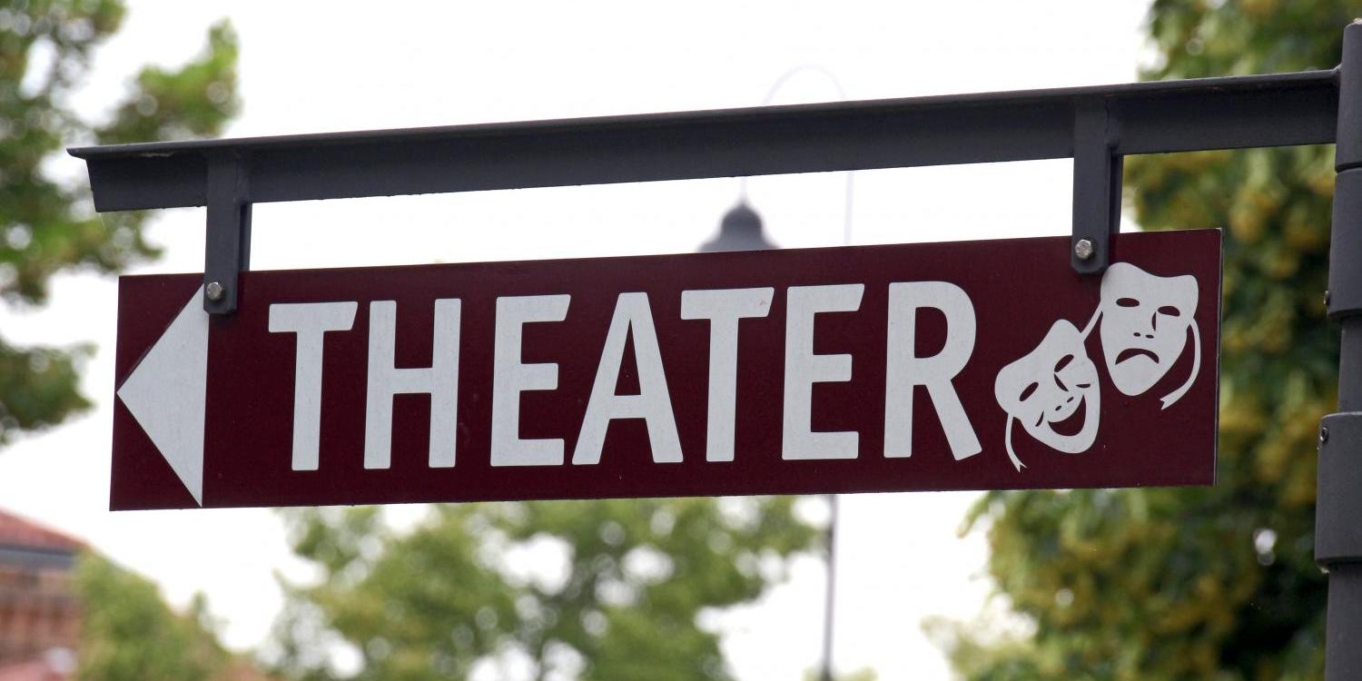 Ein Wegweiser mit der Aufschrift „THEATER“ zeigt nach links; daneben sind zwei typische Theatermasken für Komödie und Tragödie abgebildet.