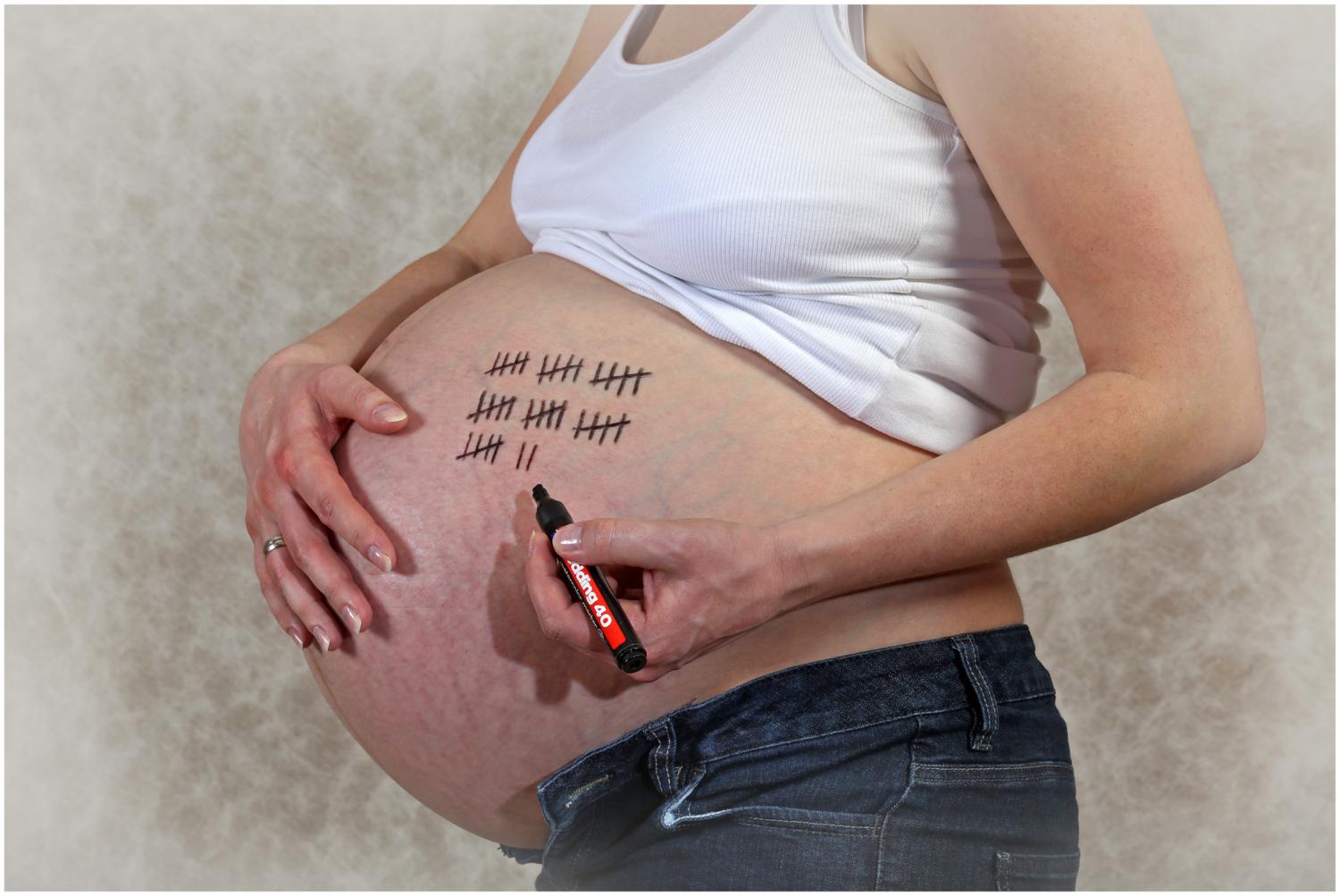 Eine schwangere Frau, die Strichlisten auf ihren Bauch malt – vermutlich zur humorvollen Darstellung der verbleibenden Wochen bis zur Geburt.