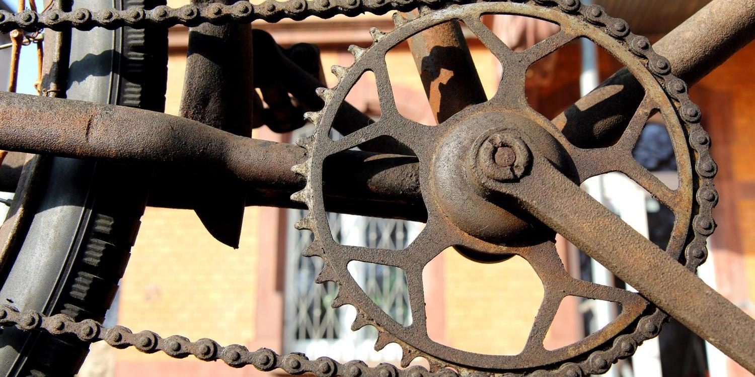 Das Bild zeigt eine rostige Fahrradkette, ein großes Kettenrad und Teile des Hinterrads, alles stark verrostet und verwittert.