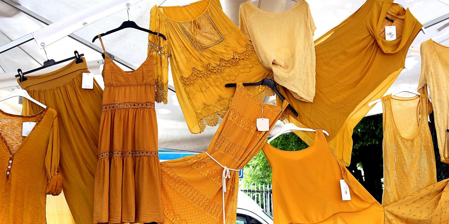 Kleider, Tops und Röcke – hängen dicht nebeneinander an einem Marktstand.