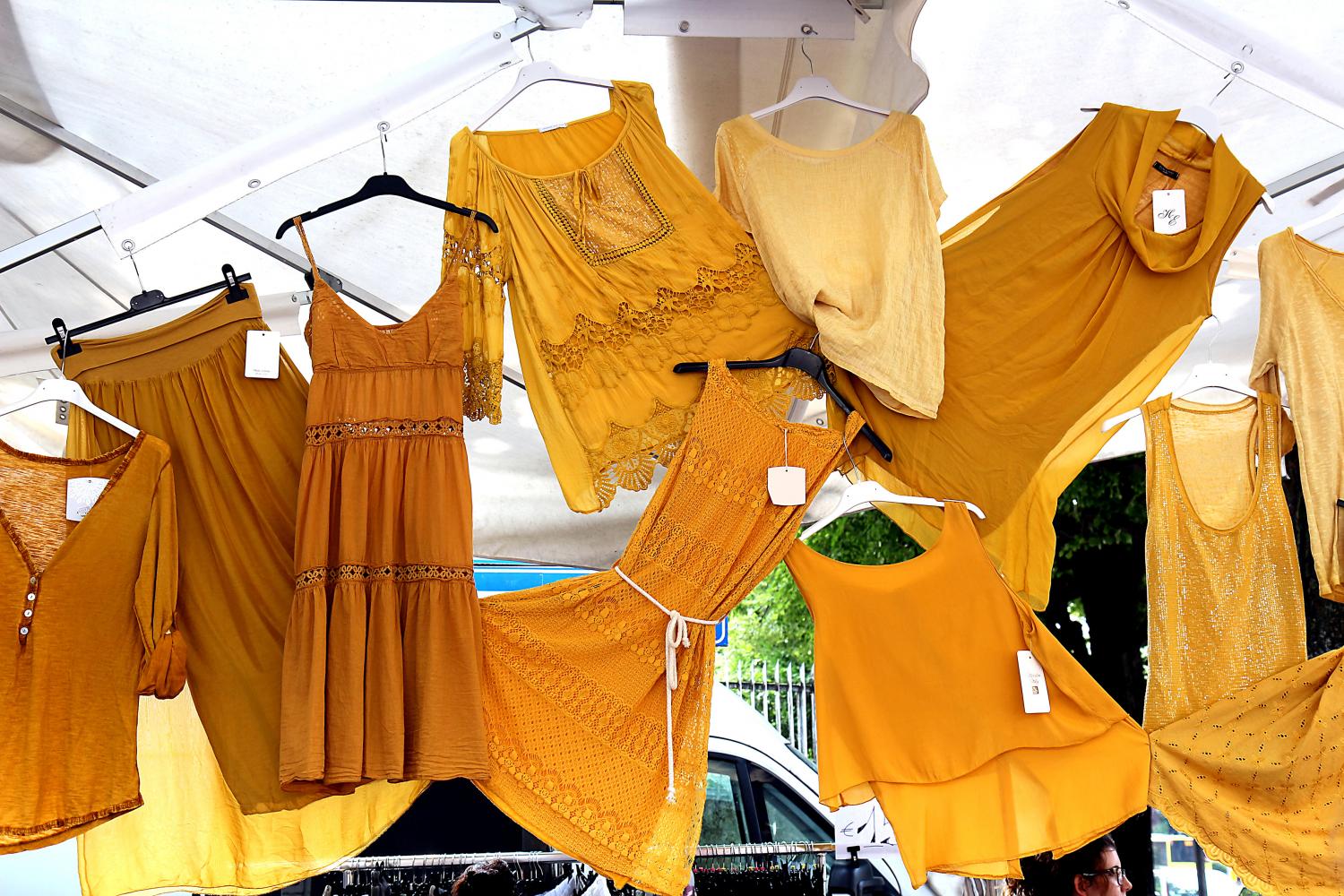 Kleider, Tops und Röcke – hängen dicht nebeneinander an einem Marktstand.