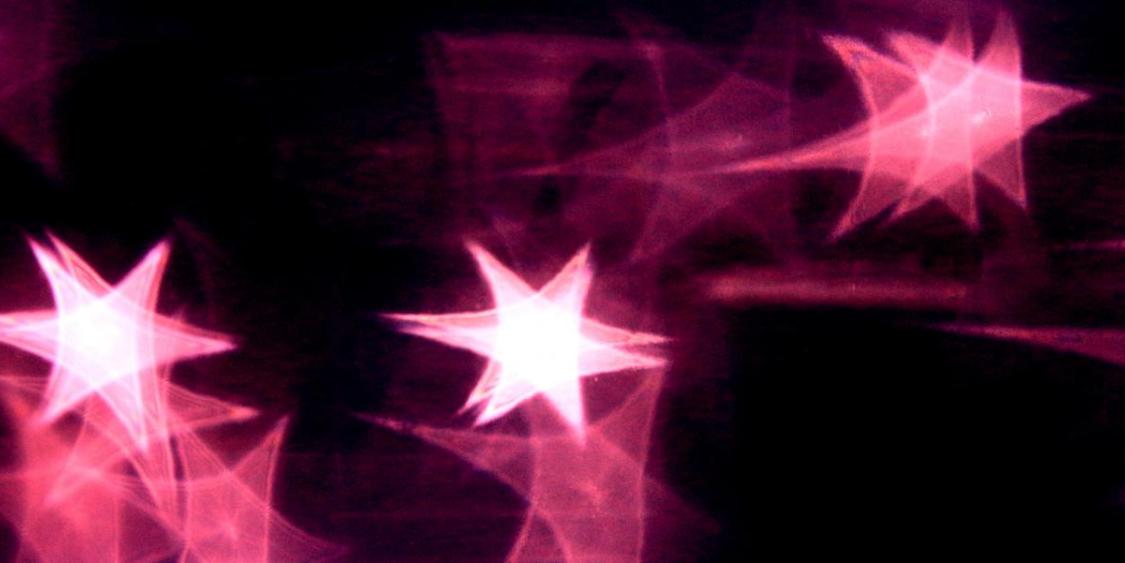 Das Bild zeigt mehrere leuchtende, pink-violette Sterne auf dunklem Hintergrund.