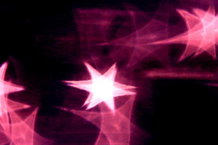 Das Bild zeigt mehrere leuchtende, pink-violette Sterne auf dunklem Hintergrund.