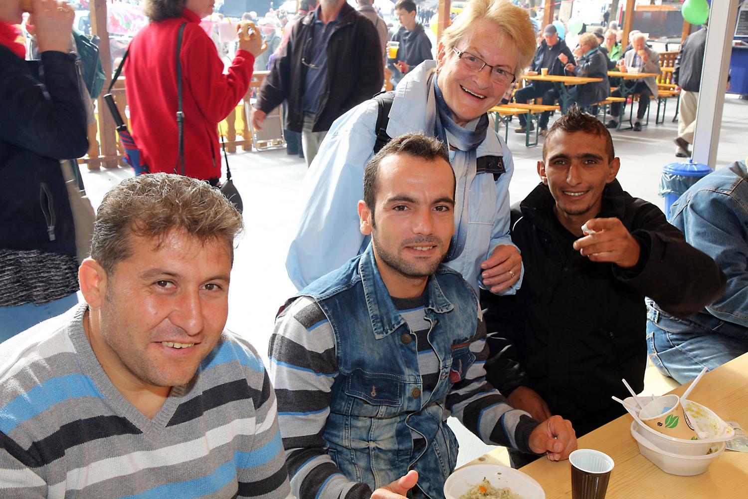 Eine kleine Gruppe von Menschen sitzt und steht gemütlich an Tischen bei einer Essens‑ oder Gemeinschaftsveranstaltung.
