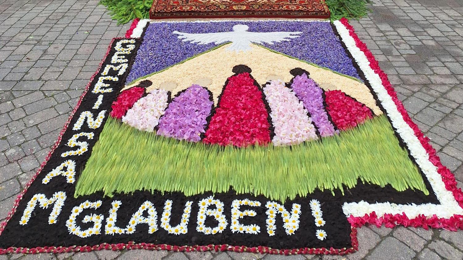 Blumenteppich vor einem festlich geschmückten Altar im Freien, mit Kreuz und Blumen.