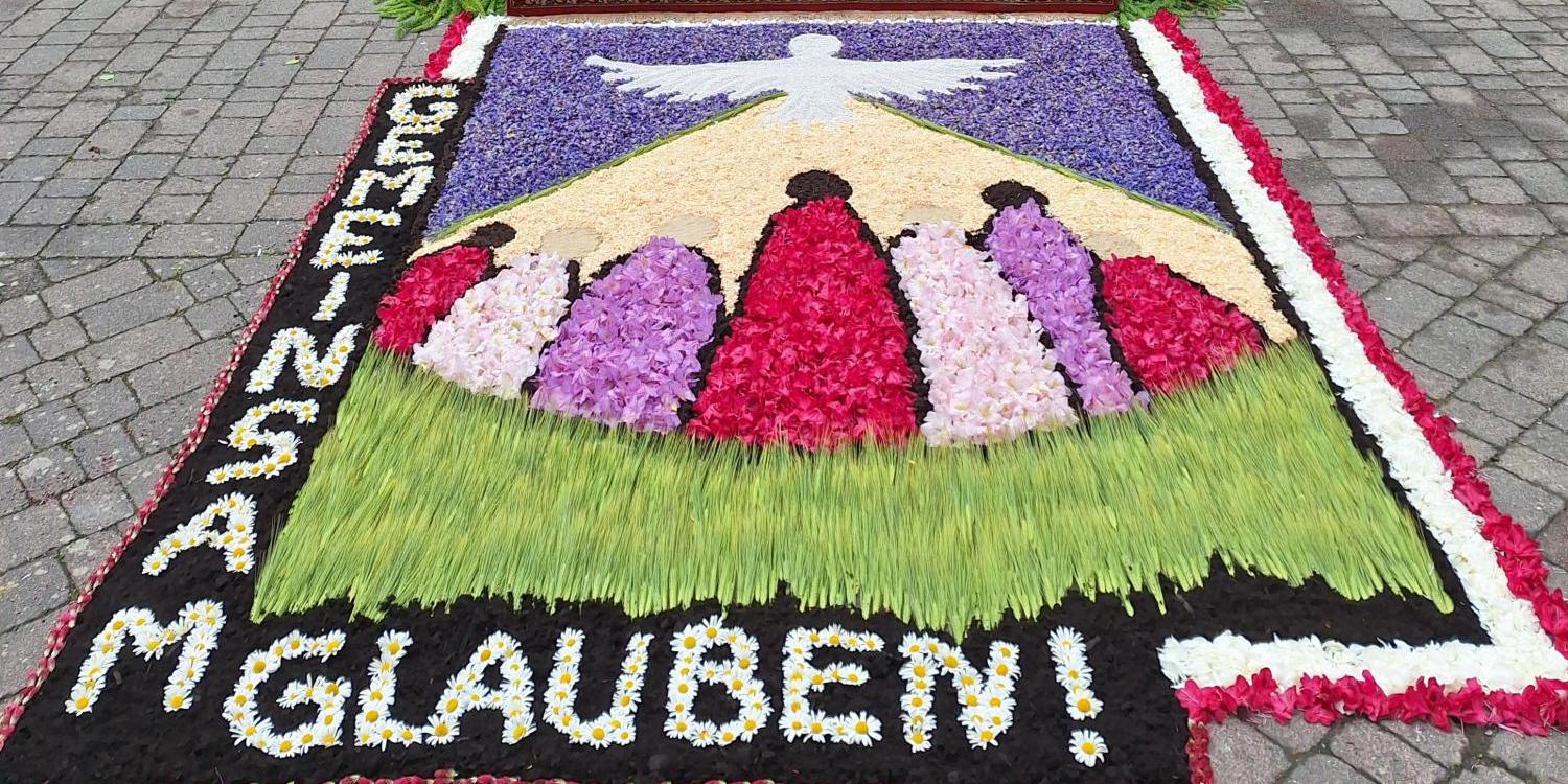 Blumenteppich vor einem festlich geschmückten Altar im Freien, mit Kreuz und Blumen.