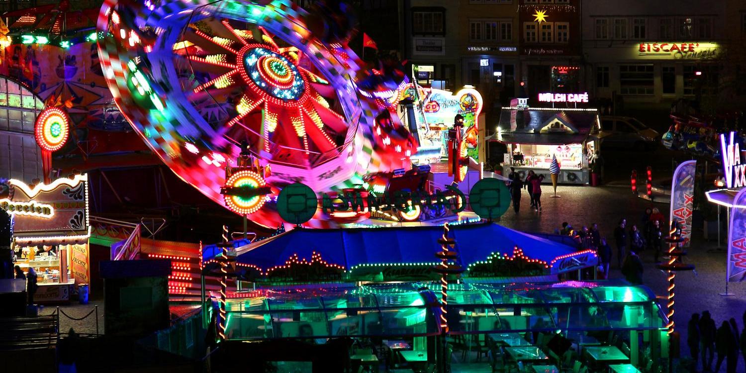 Bunter Jahrmarkt bei Nacht mit hell erleuchtetem Fahrgeschäft und leeren Tischen im Vordergrund. (c) Bild: Peter Weidemann In: Pfarrbriefservice.de Bunter Jahrmarkt bei Nacht mit hell erleuchtetem Fahrgeschäft und leeren Tischen im Vordergrund.