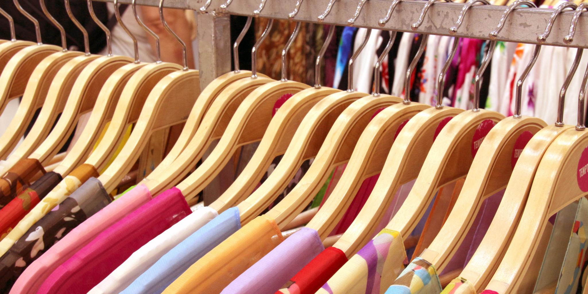 Kleider auf Holzkleiderbügeln an einer Kleiderstange, verschiedene Farben und Muster.
