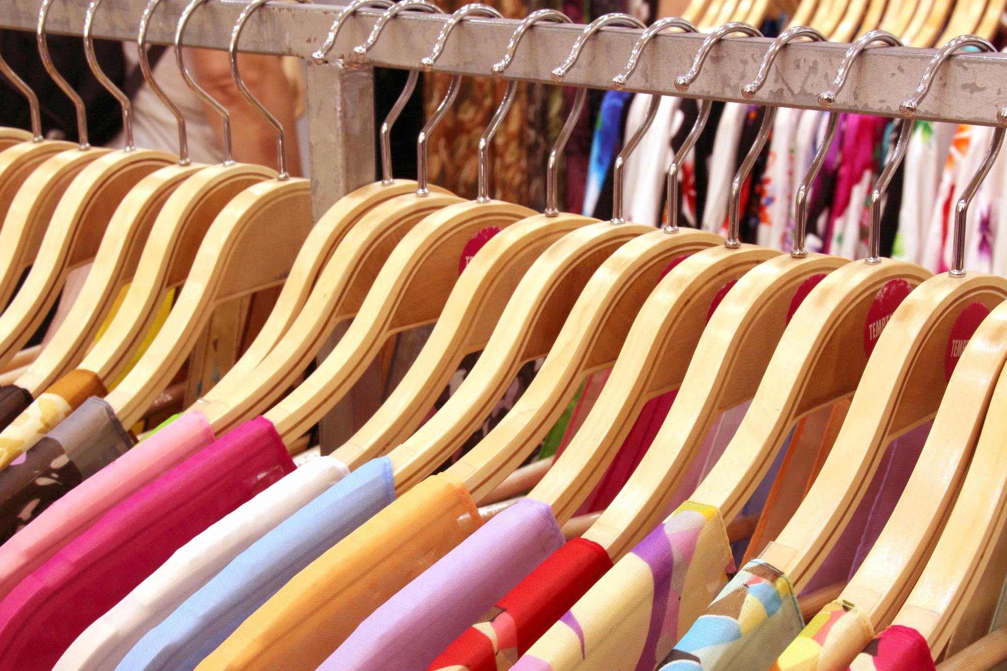 Kleider auf Holzkleiderbügeln an einer Kleiderstange, verschiedene Farben und Muster.
