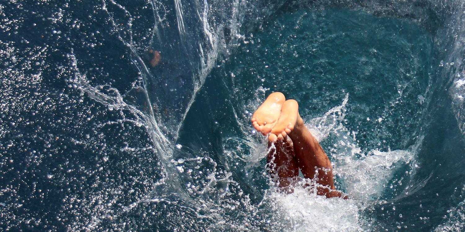 Ein Mensch taucht kopfüber ins Wasser ein und erzeugt dabei einen großen Spritzer