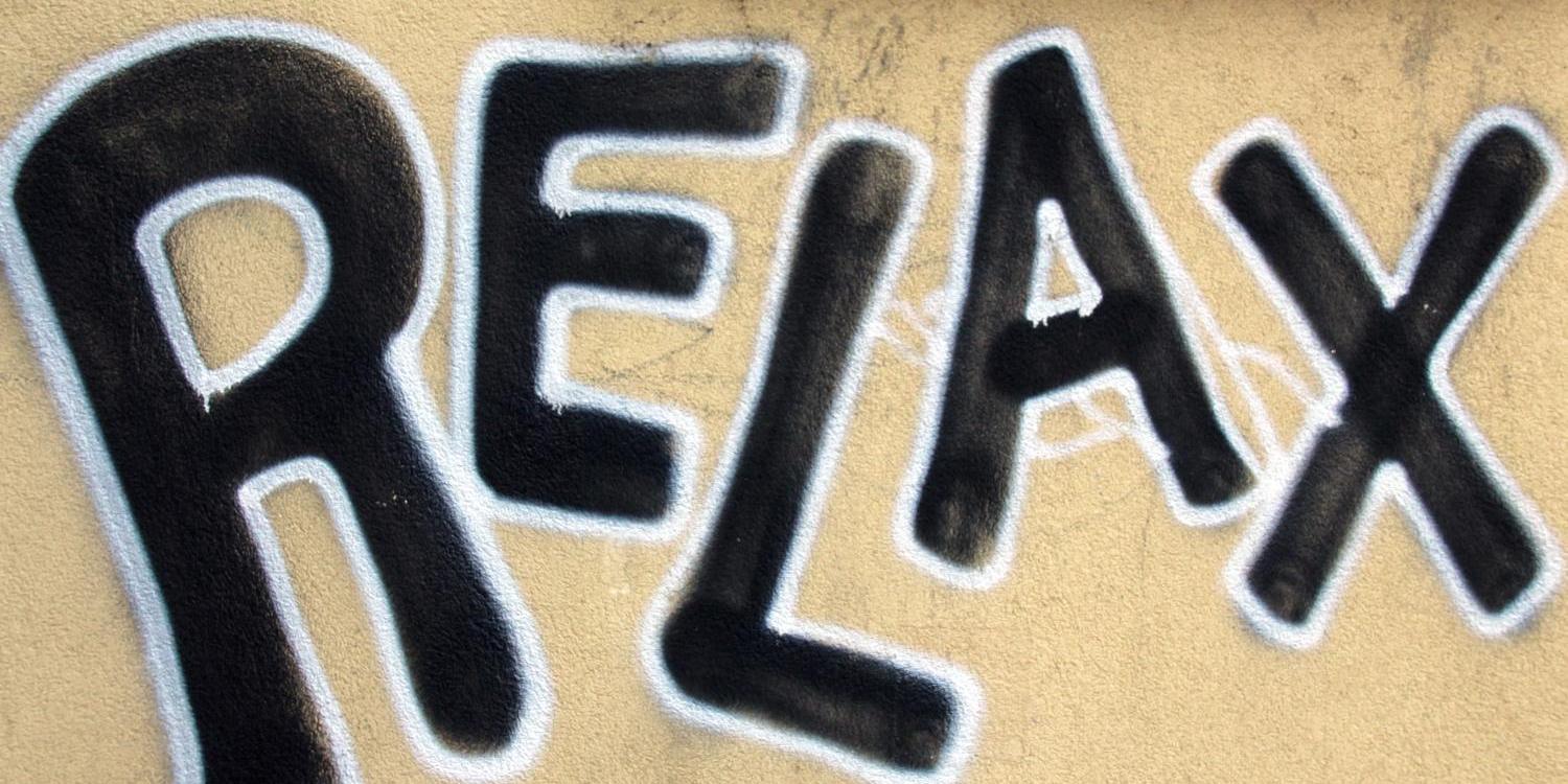 Ein großes Graffiti mit dem Wort „RELAX“ in schwarzen Buchstaben mit heller Kontur auf einer Wand.