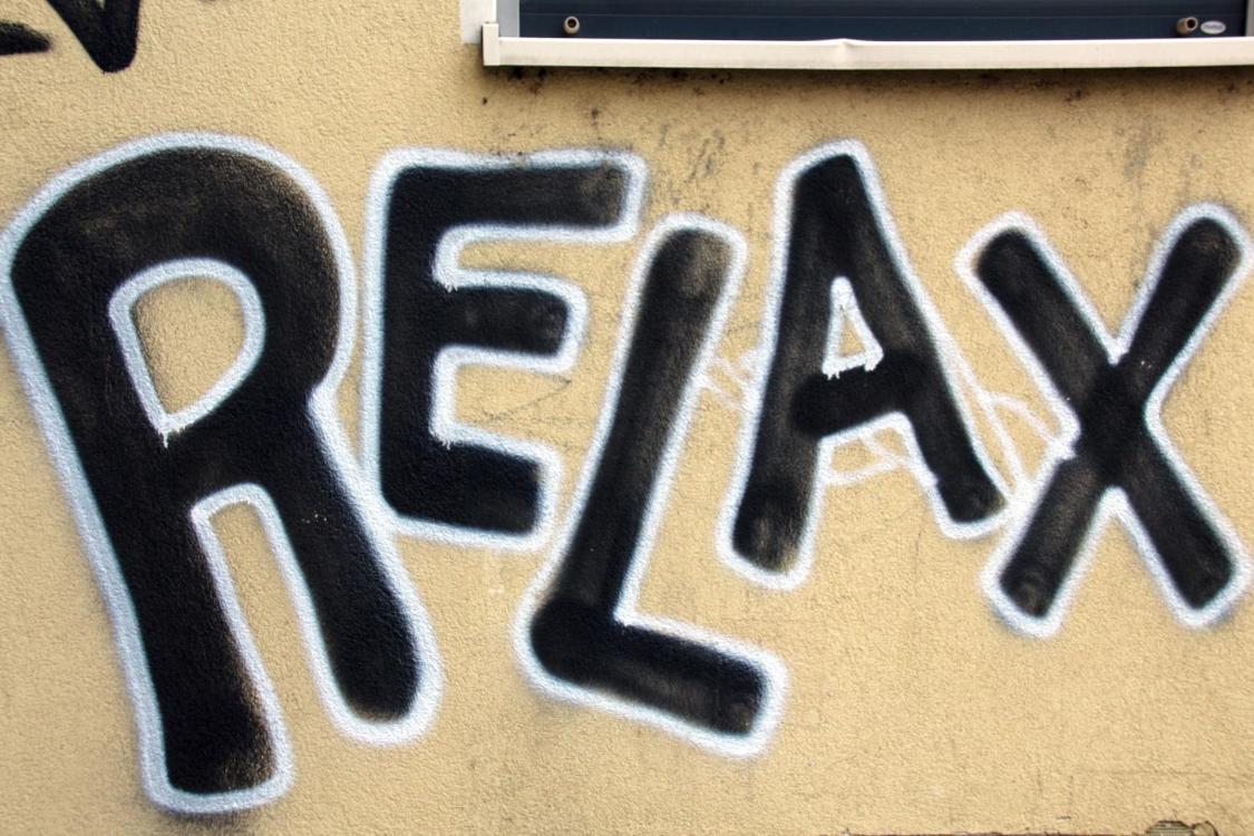 Ein großes Graffiti mit dem Wort „RELAX“ in schwarzen Buchstaben mit heller Kontur auf einer Wand.