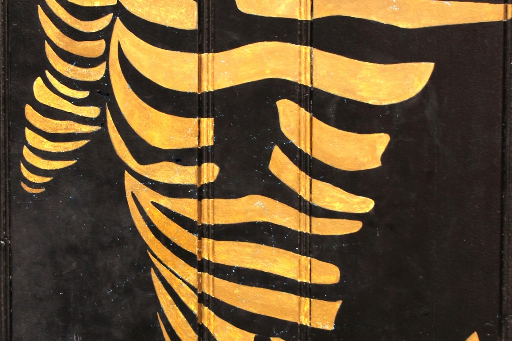 Das Foto zeigt eine stilisierte goldene Figur, die aus geschwungenen Linien auf schwarzem Hintergrund gebildet ist und eine dynamische, abstrakte Körperform darstellt.