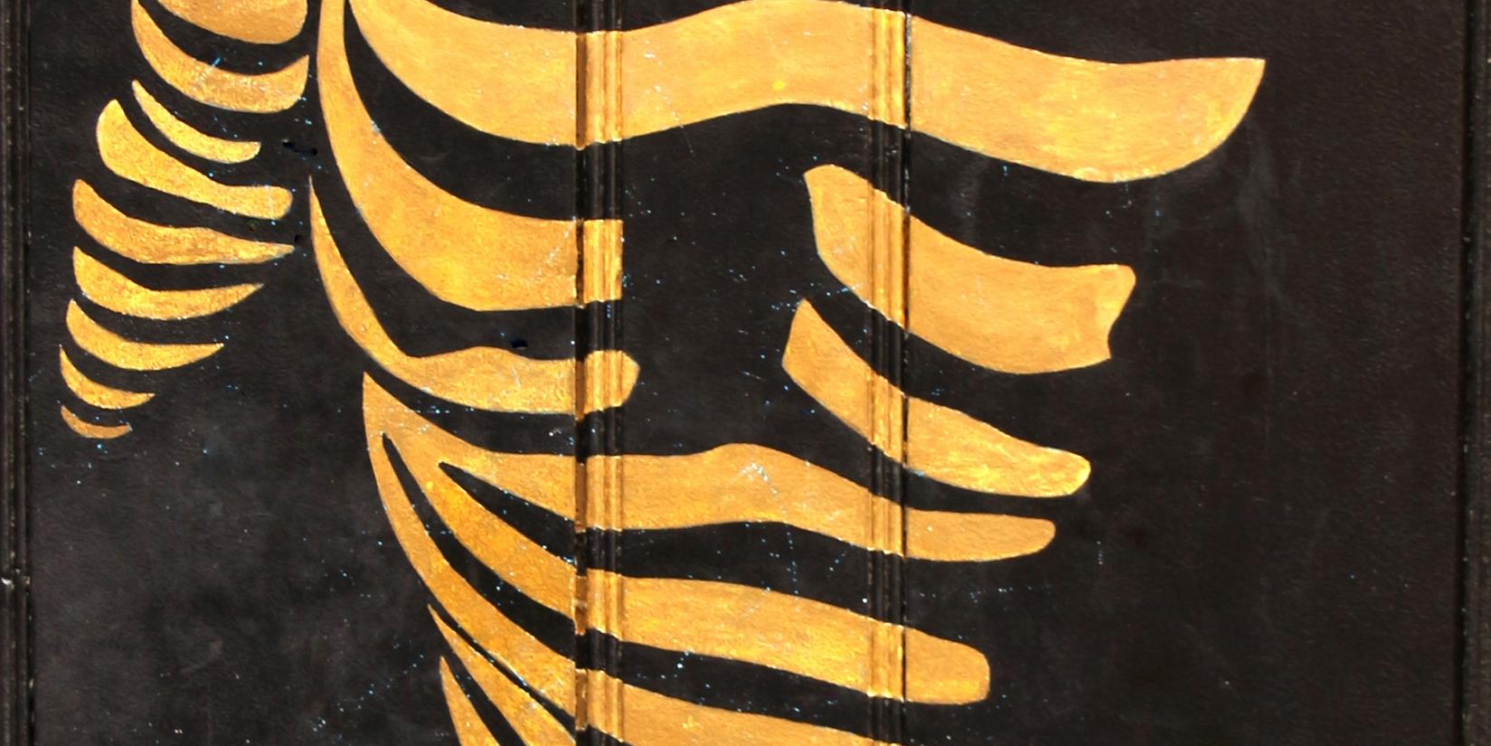 Das Foto zeigt eine stilisierte goldene Figur, die aus geschwungenen Linien auf schwarzem Hintergrund gebildet ist und eine dynamische, abstrakte Körperform darstellt.