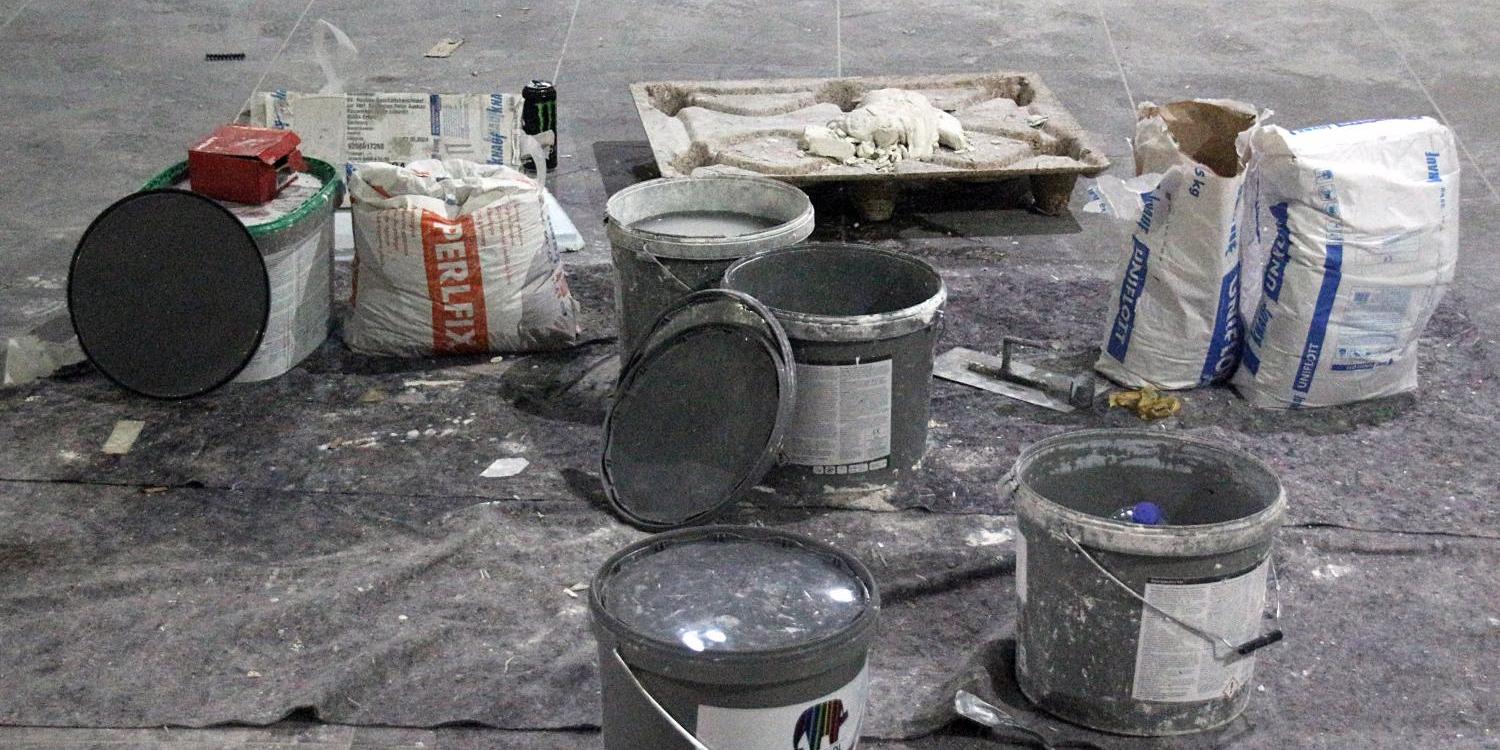 Baumaterial und Farbeimer stehen auf einer staubigen Abdeckplane.