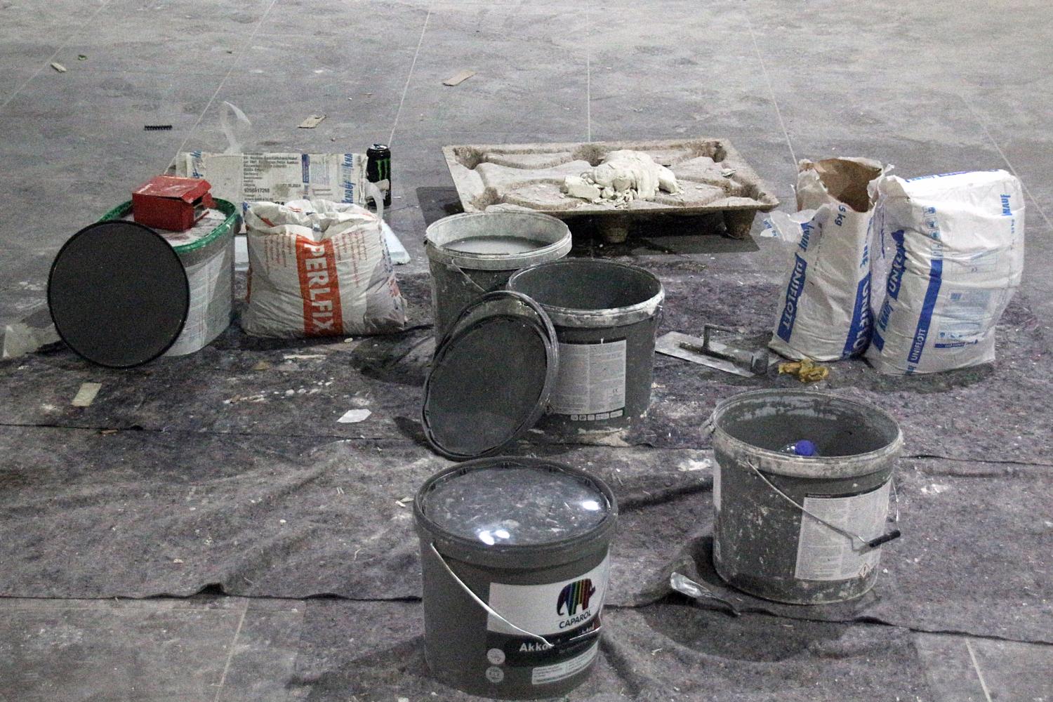Baumaterial und Farbeimer stehen auf einer staubigen Abdeckplane.