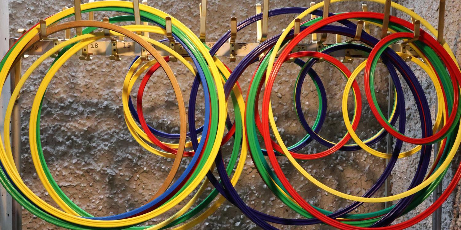 Mehrere bunte Gymnastikreifen hängen ordentlich sortiert an einer Wandhalterung.