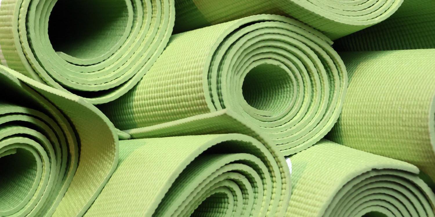 Mehrere aufgerollte grüne Gymnastikmatten liegen dicht übereinandergestapelt.