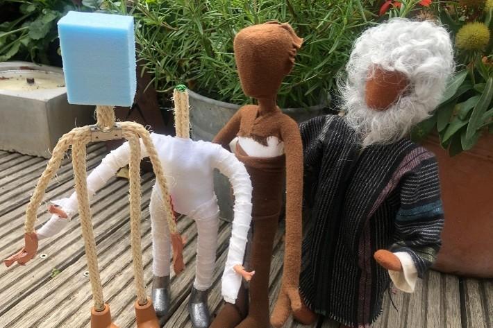Vier handgefertigte Stofffiguren stehen auf einer Holzterrasse, eine Figur hat weißes Haar und einen weißen Bart.