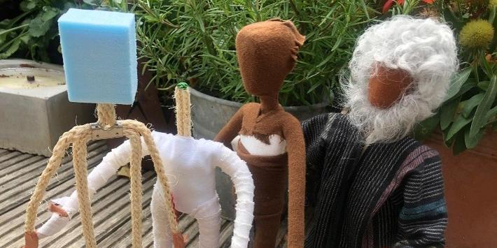 Vier handgefertigte Stofffiguren stehen auf einer Holzterrasse, eine Figur hat weißes Haar und einen weißen Bart.